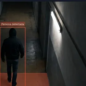 Interfaz de monitoreo con la vista de la cámara CAM 04 sobre un pasillo. Una persona camina de espaldas, sin que se vea su rostro, dentro de un recuadro rojo rotulado persona detectada, y pisa un área roja marcada como zona restringida. A la derecha, una alerta que dice acceso a zona restringida, y dos tarjetas: aviso en 1.4 segundos y 24 cámaras